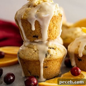 Cranberry Orange Muffins with Zesty Citrus Glaze 7 Two muffins stacked with a glaze dripping down the sides. Cranberries and oranges slices off the sides.