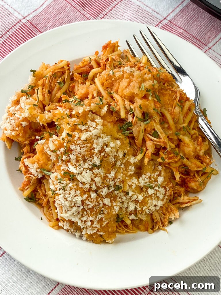 One-Pot Slow Cooker Chicken Parmesan Recipe 4 Over head view of white plate of crock pot chicken parmesan with spaghetti on a red plaid napkin