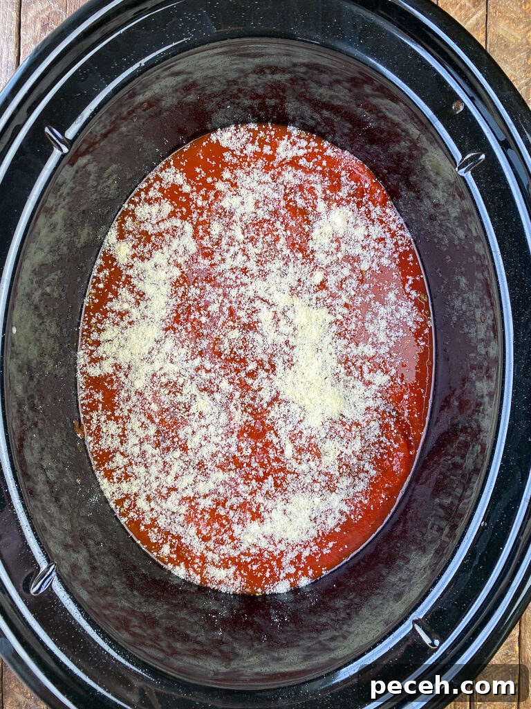 One-Pot Slow Cooker Chicken Parmesan Recipe 7 Grated parmesan cheese sprinkled on red sauce and chicken in a large black slow cooker