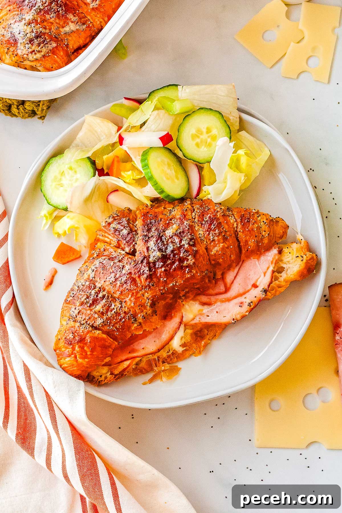 a warm ham and cheese croissant on a white plate with salad.