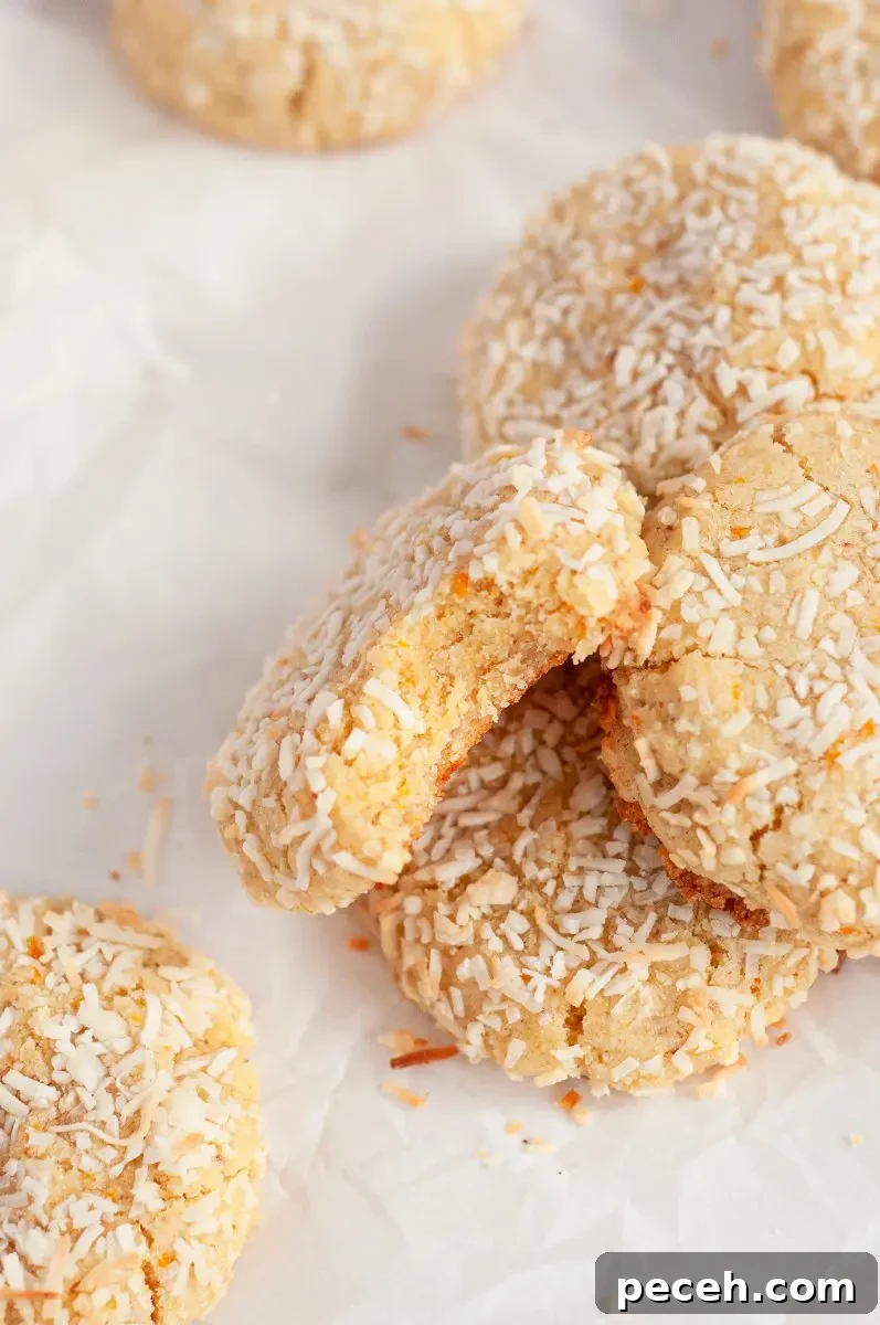Coconut orange cookies covered in white shredded coconut on a table in a haphazard line. One cookie has a large bite taken out of it and is facing towards the camera.