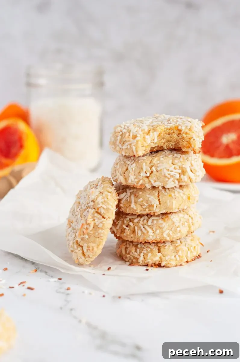 A tall stack of coconut orange cookies that are covered in white shredded coconut. The top cookie has a bite taken out of it.