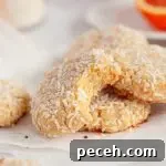 Coconut orange cookies covered in shredded white coconut. There is a cookie in front with a bite taken out of it leaning up against the other cookies.
