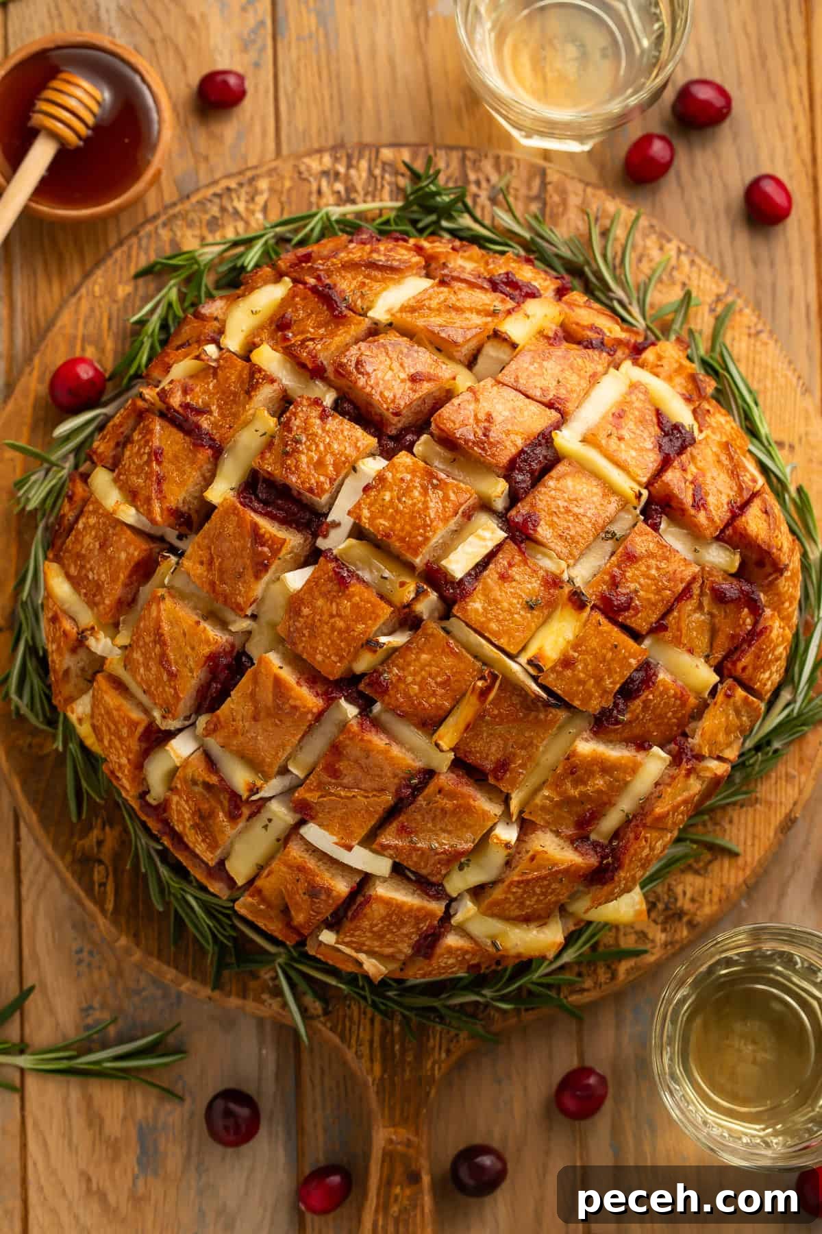 Cranberry and Brie Pull-Apart Bread 2 Top down view of a cranberry brie pull apart bread on a wooden board garnished with rosemary sprigs around it like a wreath.