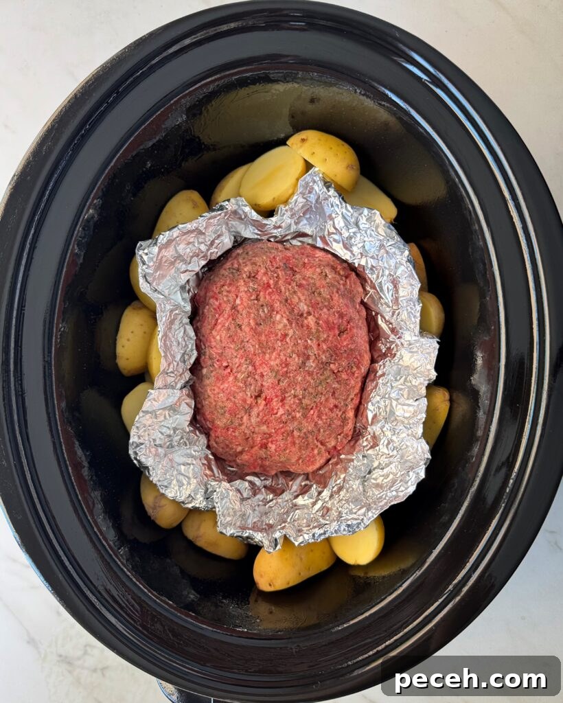 overhead shot of uncooked meatloaf and potatoes in a black slow cooker