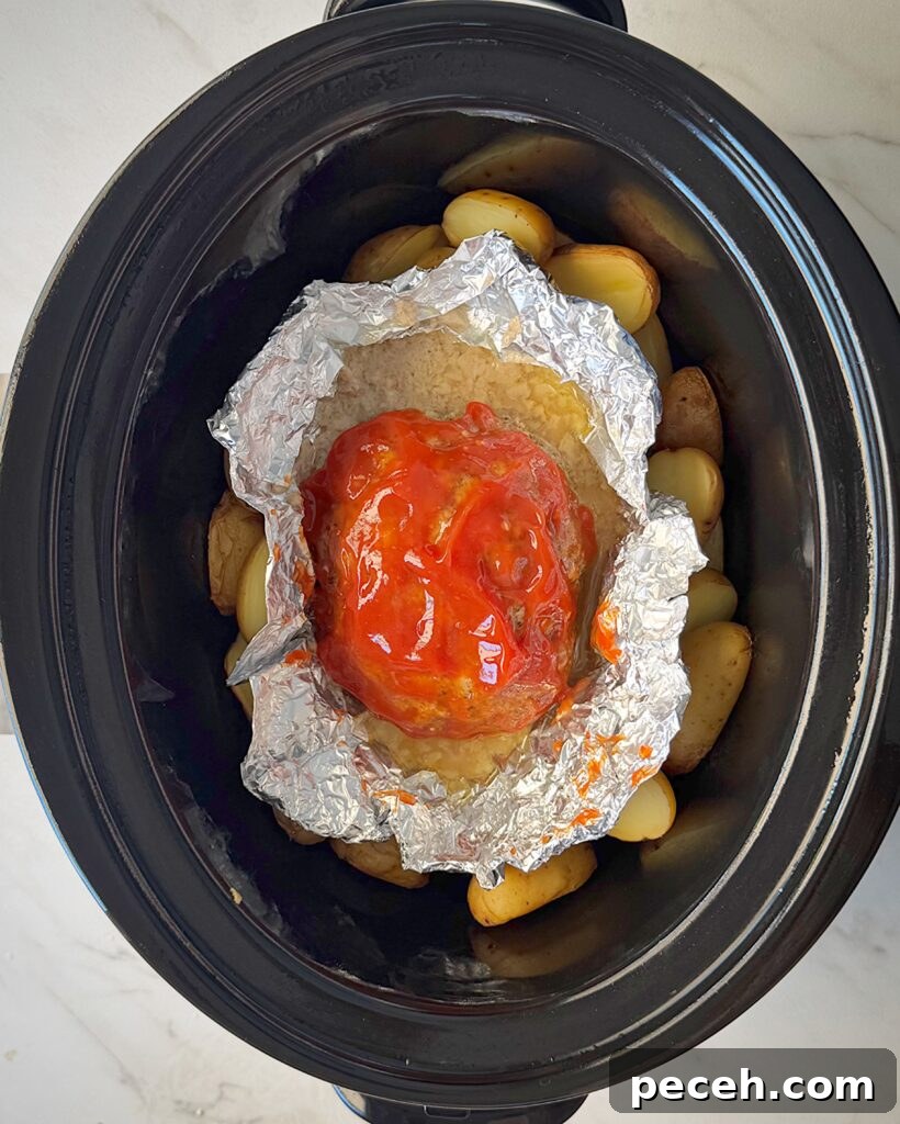 overhead shot of cooked meatloaf and potatoes in a black slow cooker