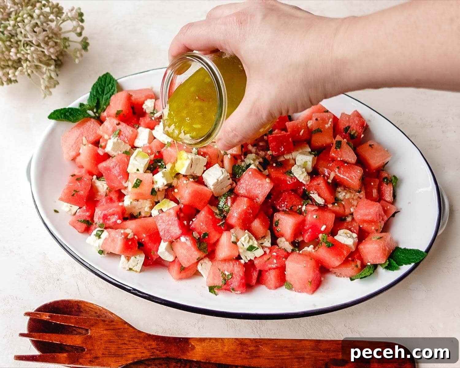 Pouring salad dressing over watermelon feta salad with mint.