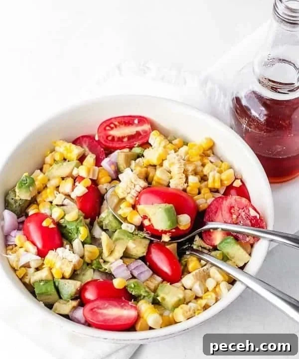 Avocado Corn Tomato salad with red onion ready to be eaten with two spoons in the bowl and dressing on the side ready to be poured in