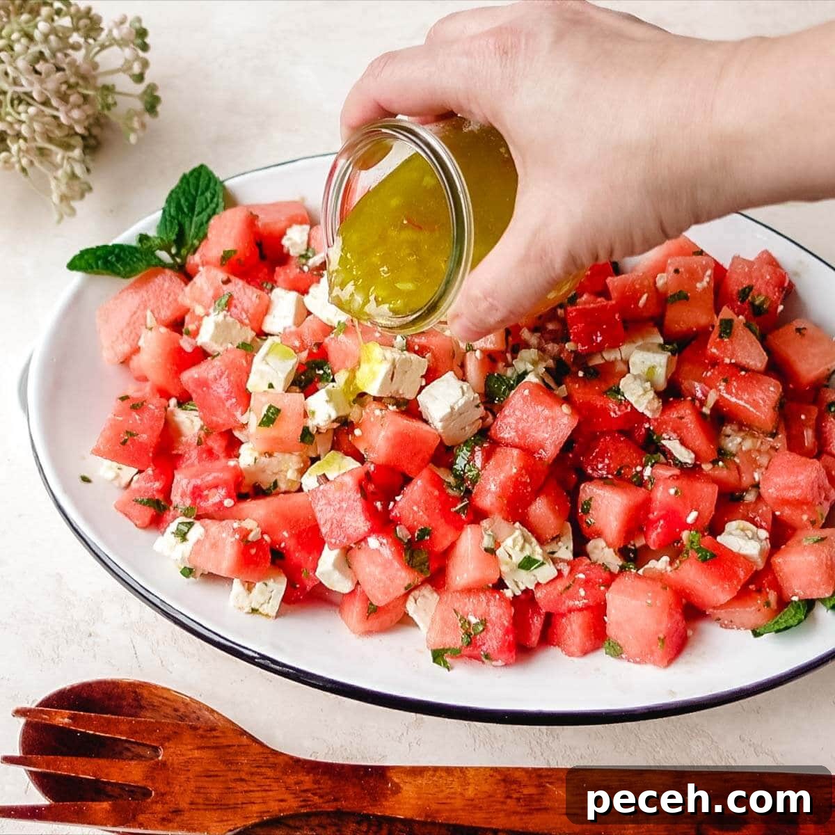 Hand pouring citrus mint dressing over a watermelon feta salad.