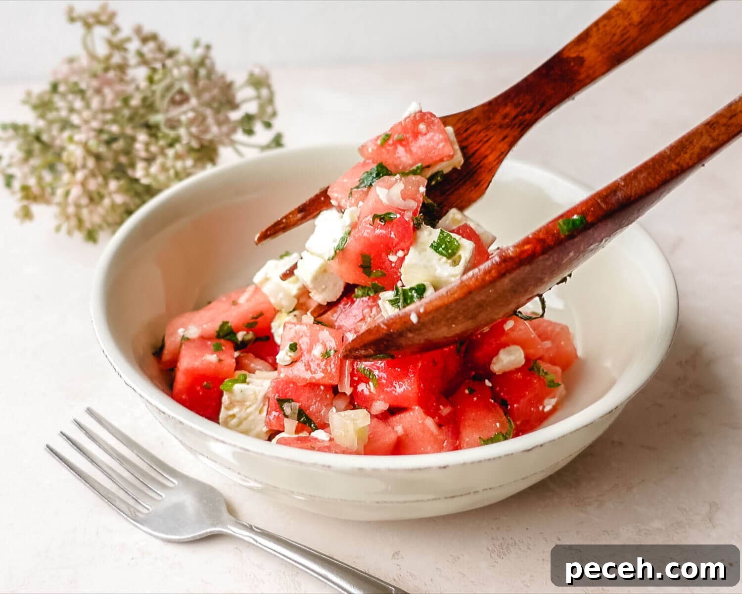 Using salad tongs to serve watermelon feta salad with mint.