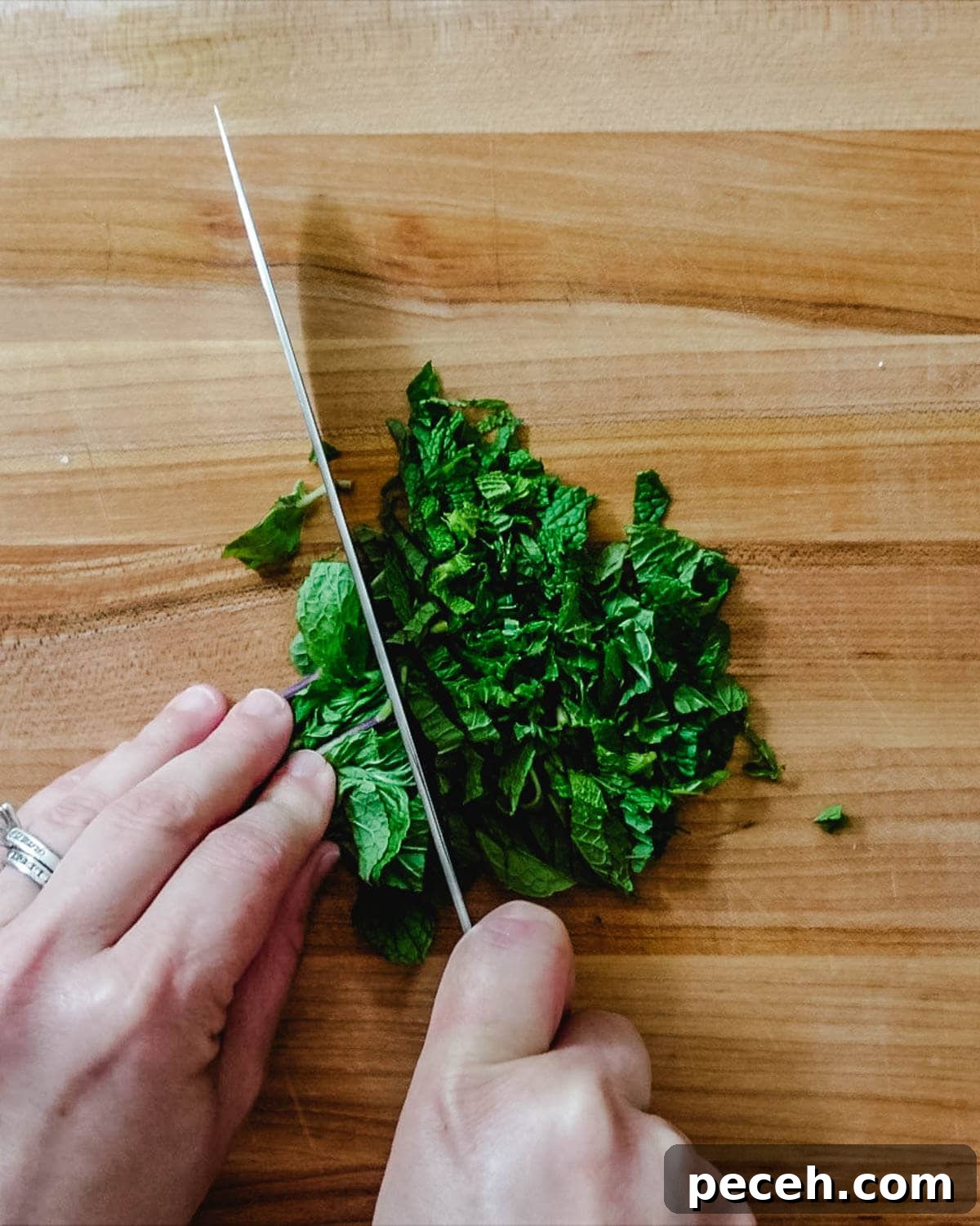 Hand chopping fresh mint on a wooden cutting board.
