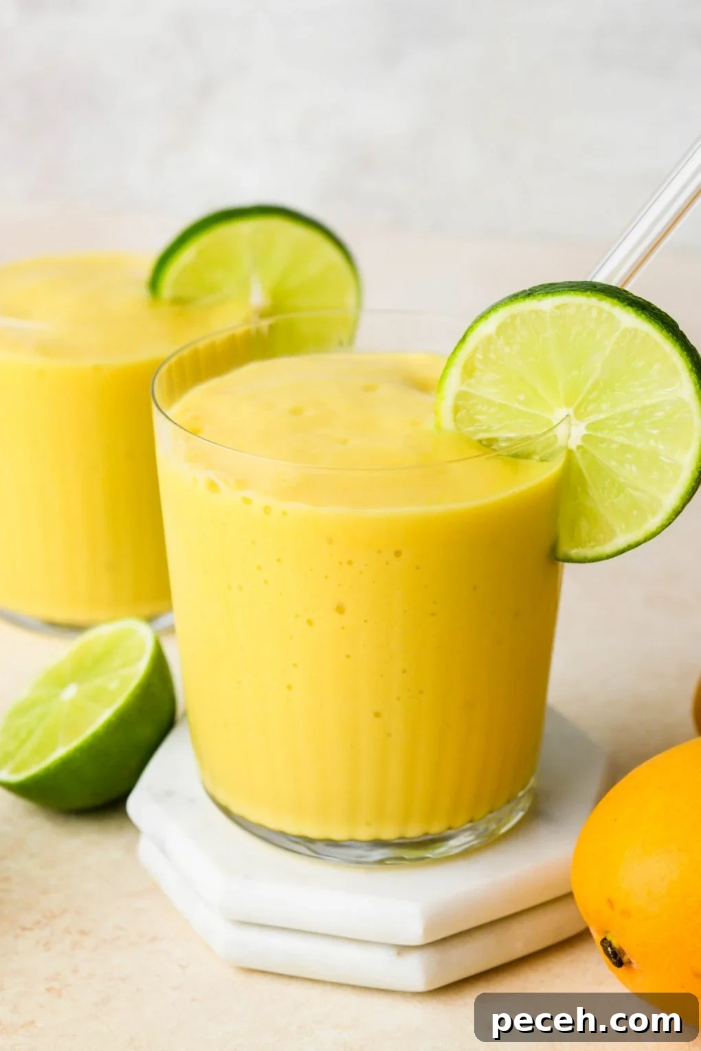 5-Minute Dairy-Free Frozen Mango Smoothie Recipe 2 Mango smoothie in a glass with a glass straw, garnished with a lime wheel.
