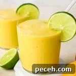 Mango smoothie in a glass with a glass straw, garnished with a lime wheel.