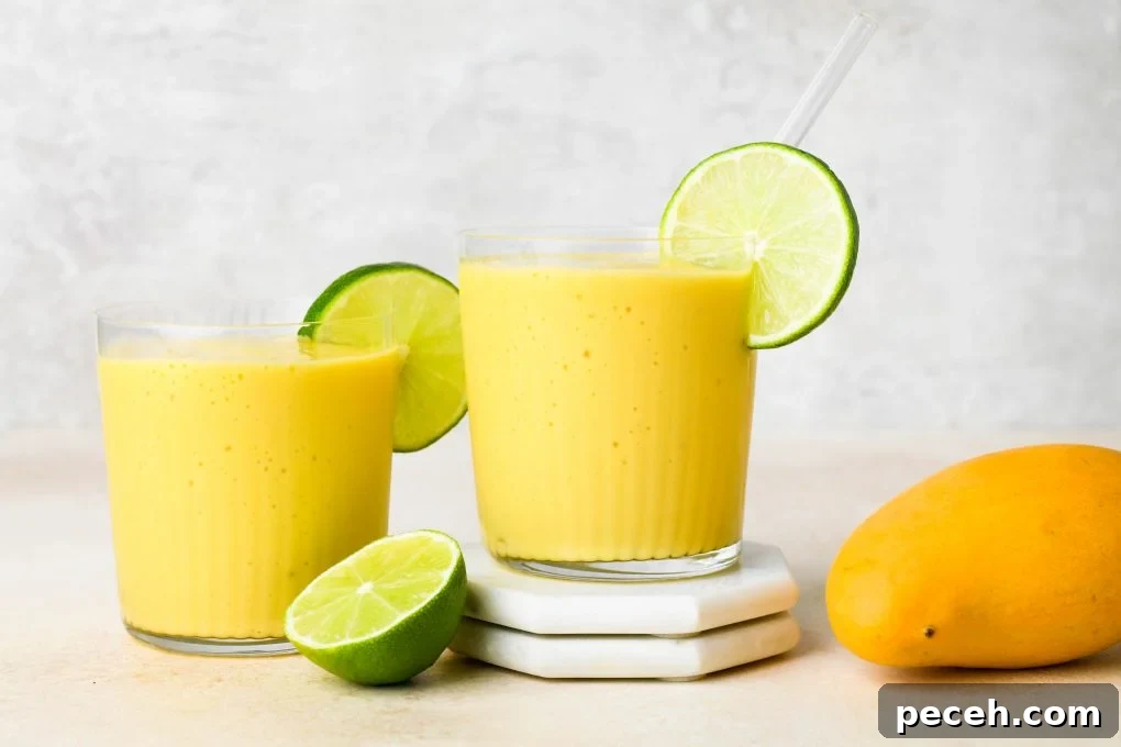 5-Minute Dairy-Free Frozen Mango Smoothie Recipe 3 Two side by side mango smoothies in a glasses with glass straws, garnished with lime wheels.