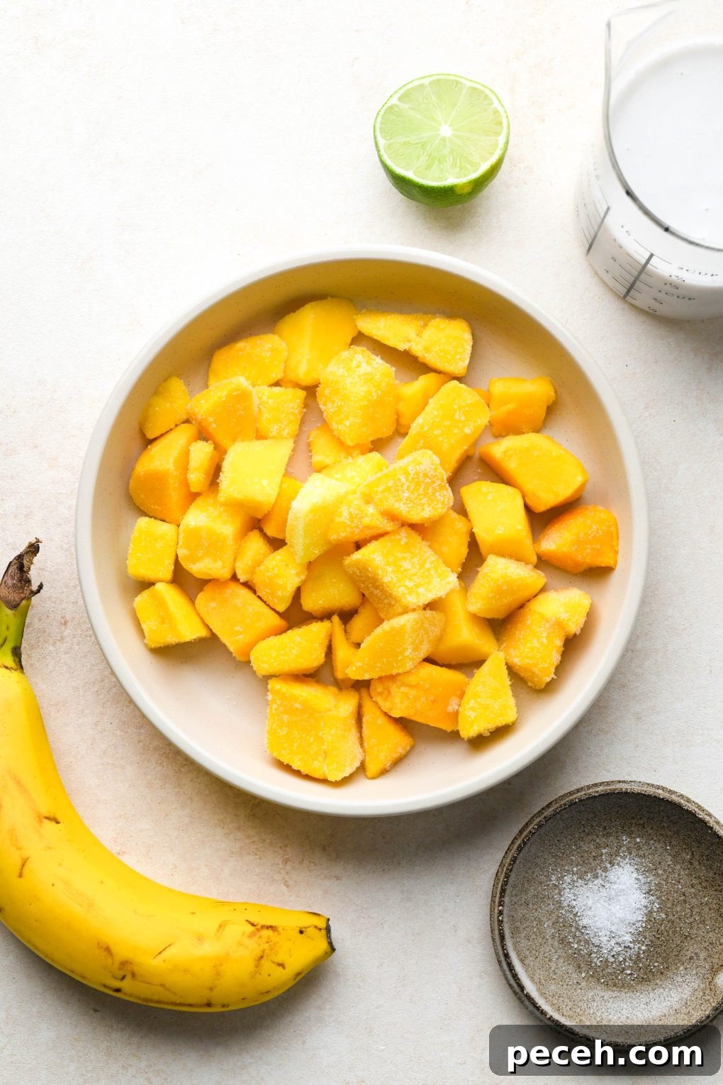 5-Minute Dairy-Free Frozen Mango Smoothie Recipe 4 Ingredients for simple mango smoothies in various ceramics, on a cream colored background.