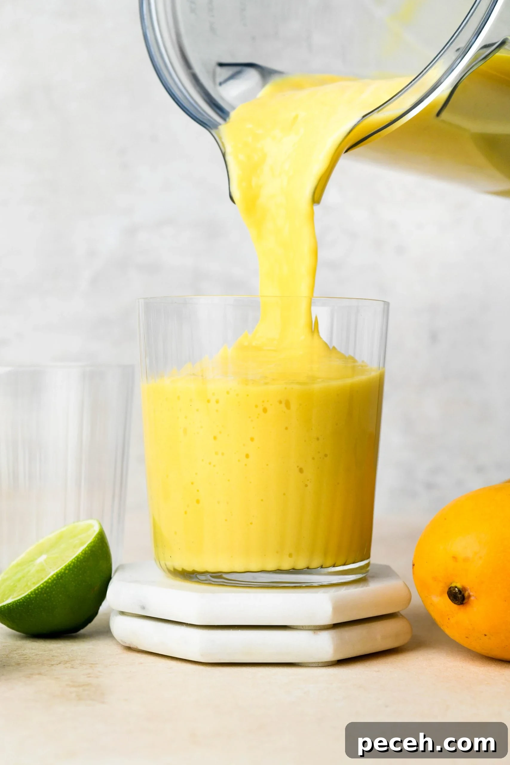 5-Minute Dairy-Free Frozen Mango Smoothie Recipe 8 How to make a simple mango smoothie: pouring mango smoothie into a cup, next to half a lime and a fresh mango.