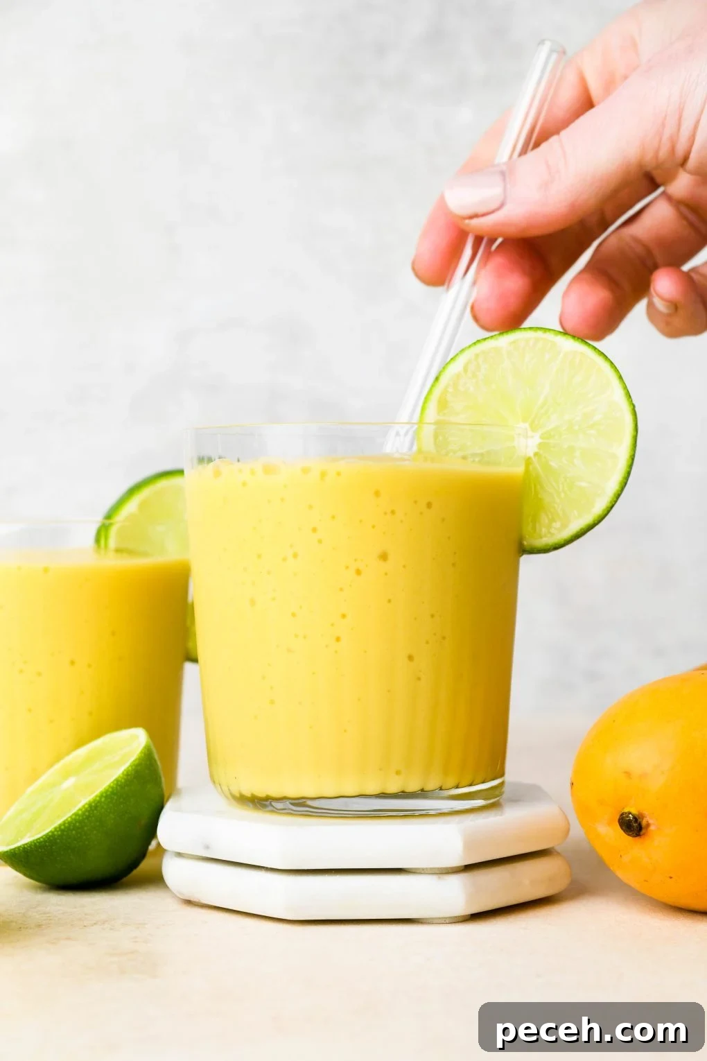 5-Minute Dairy-Free Frozen Mango Smoothie Recipe 9 A hand placing a glass straw in a glass of mango smoothie.