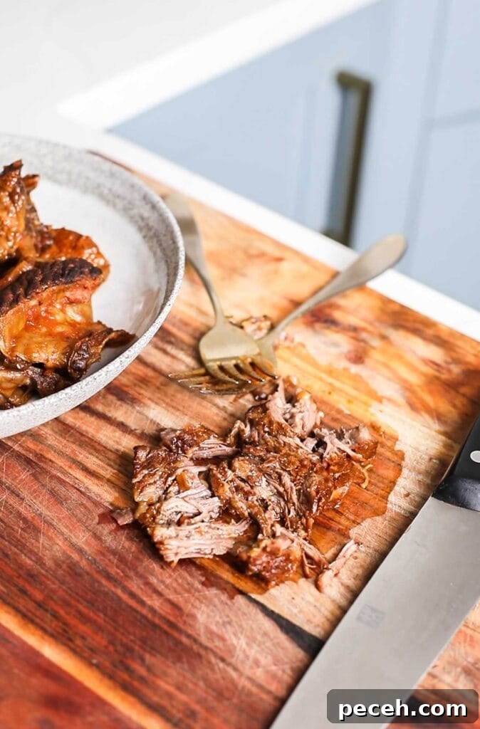 Braised Beef Short Rib Ragu Recipe — Slow-Cooked Italian Comfort 10 Showing the ribs being shredded with two forks on a cutting board.