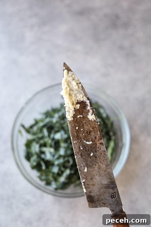 garlic paste on a knife over a bowl of kale