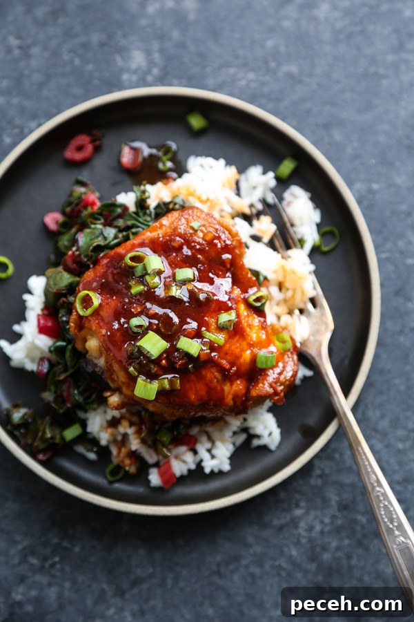 saucy chicken thighs on rice, chard, on a black plate