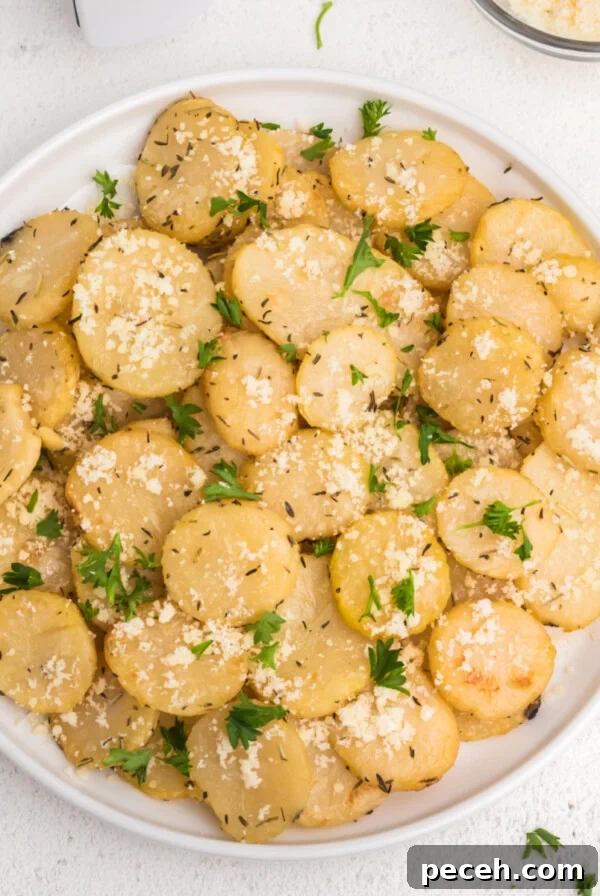 Air fryer sliced potatoes on a white plate topped with parmesan and fresh chopped parsley.