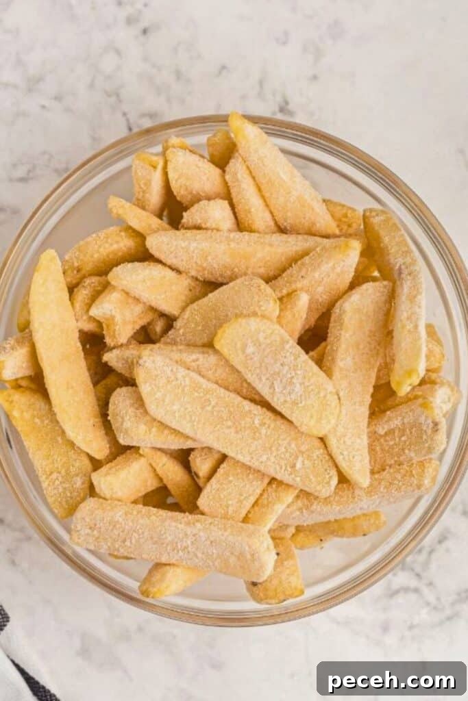 Frozen steak fries in a clear glass bowl on a marble table.