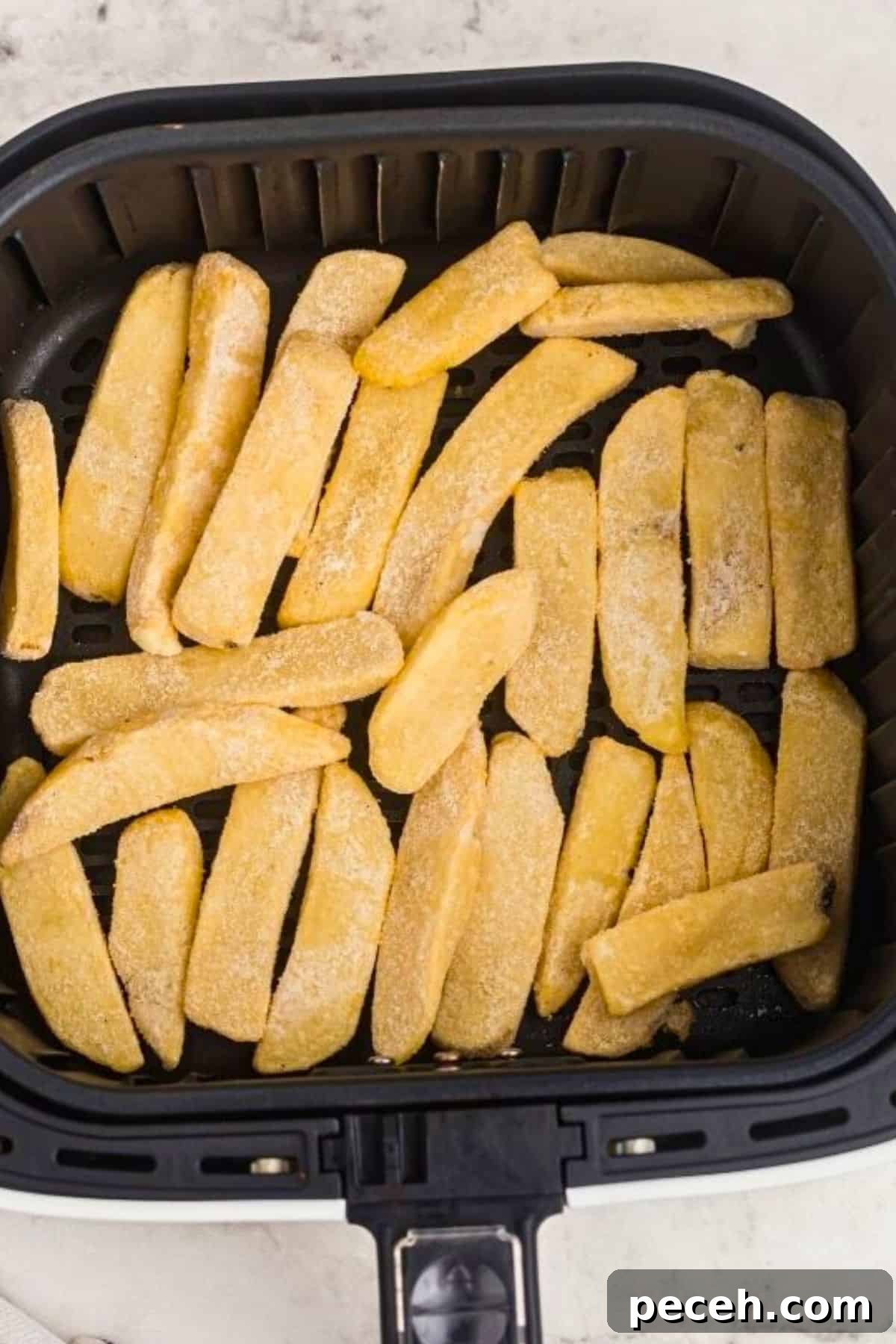 Frozen steak fries in the air fryer basket before being cooked.