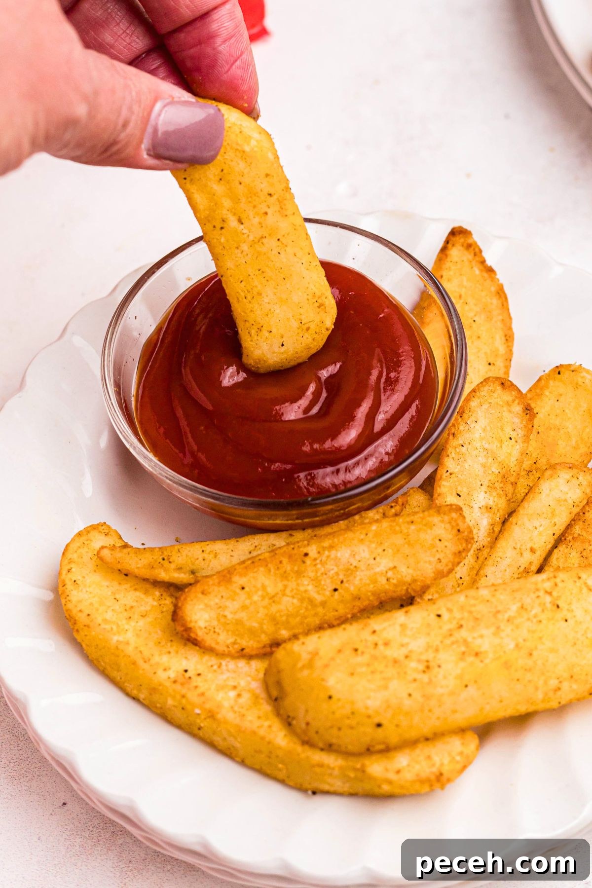 Air fryer steak fries with a hand dipping one in some ketchup.