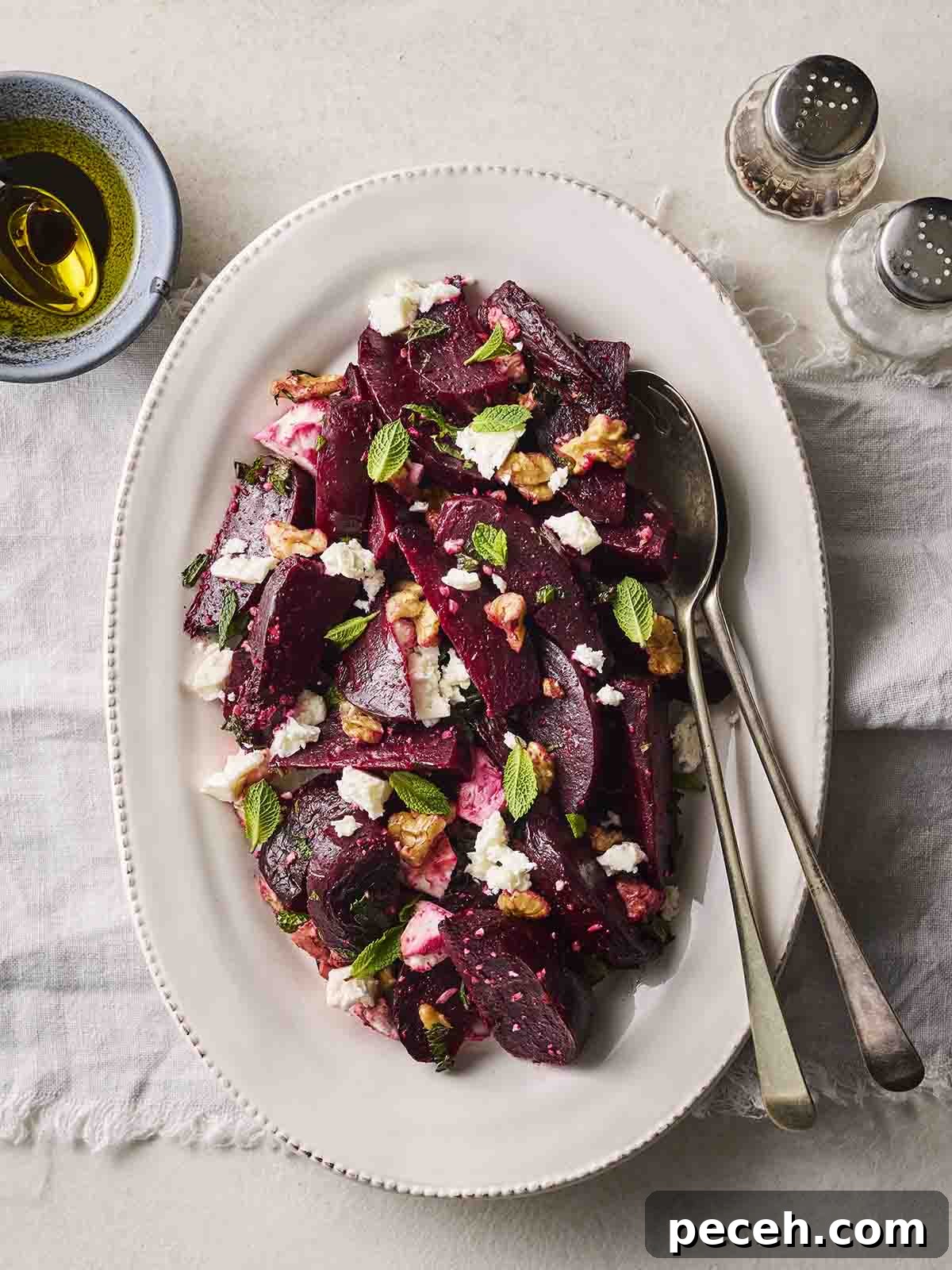 A white serving dish with a homemade Beetroot Salad on, with serving cutlery and dressing to the side.