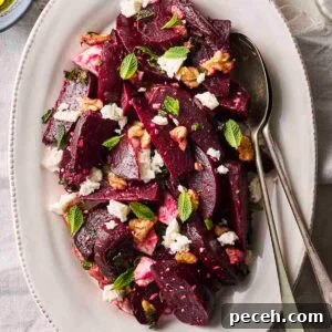 A colourful Beet Salad on a white serving plate with cutlery to serve.