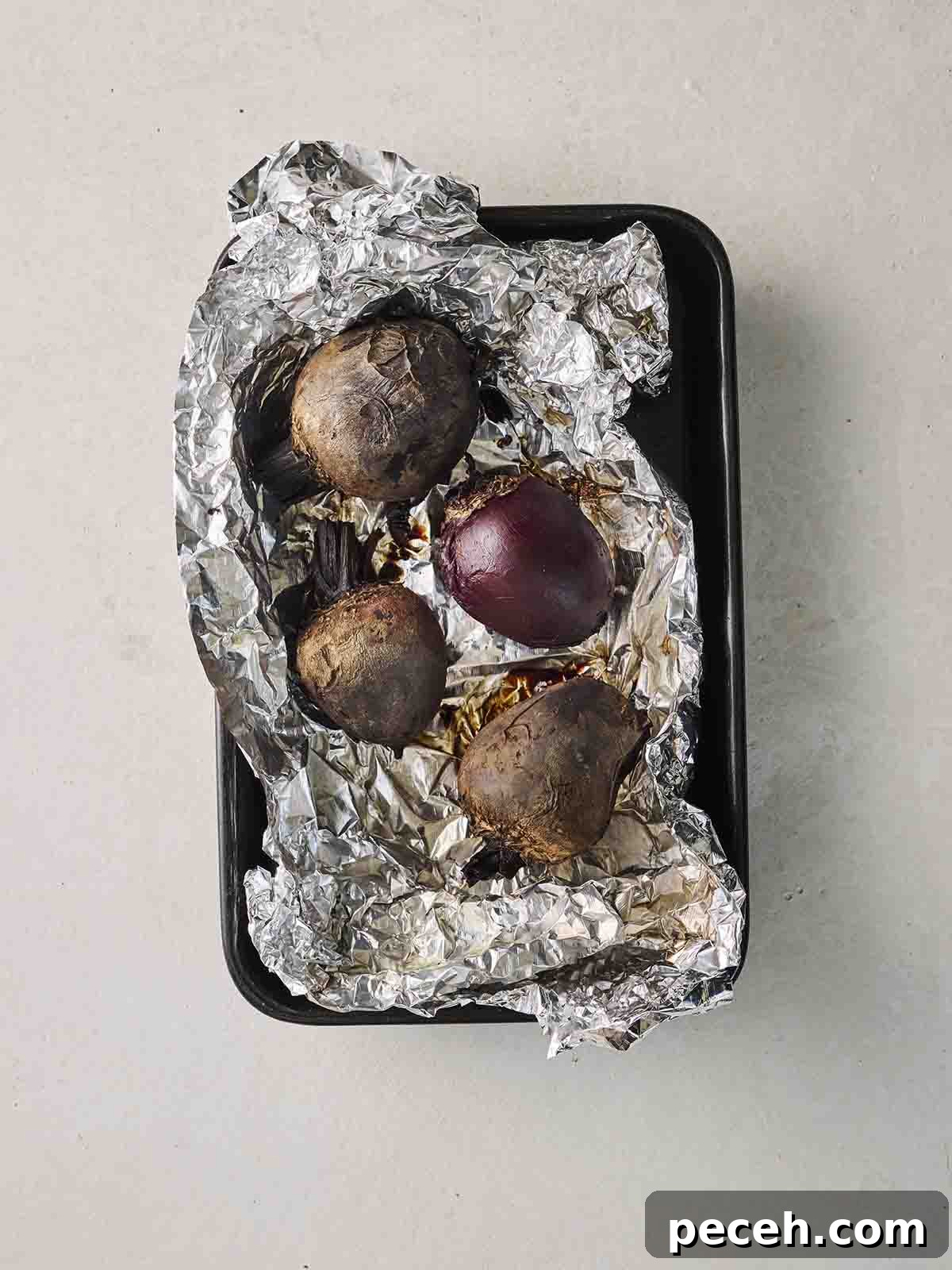 Four whole raw beetroots in top of foil in a baking tin, ready for roasting.