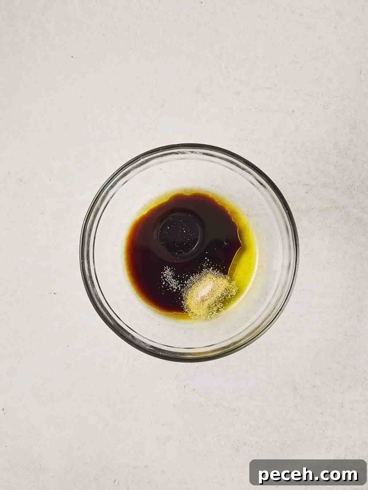 A glass bowl of olive oil, balsamic vinegar, garlic granules, salt and pepper.