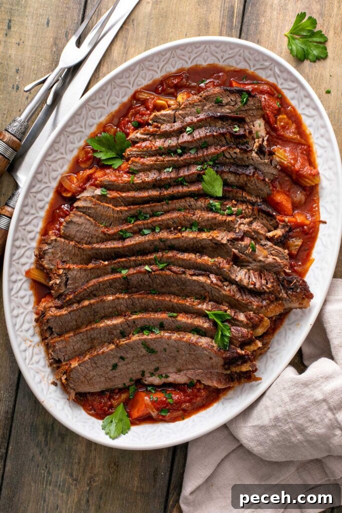 Top view of a platter filled with sliced brisket on top of carrots, onions and tomato based sauce