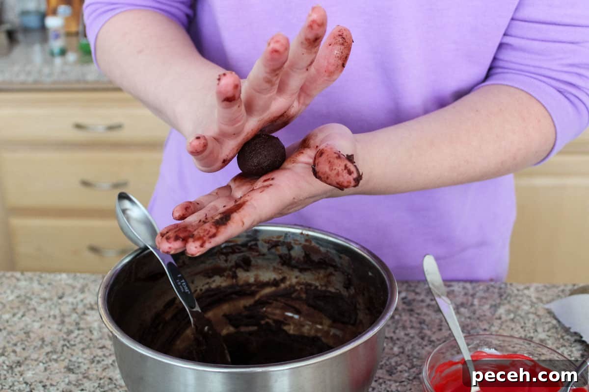 Decadent Christmas Truffles: Festive Homemade Chocolate Treats 7 A tablespoon measuring spoon in a bowl of ganache, with someone rolling a ball of one between their hands.