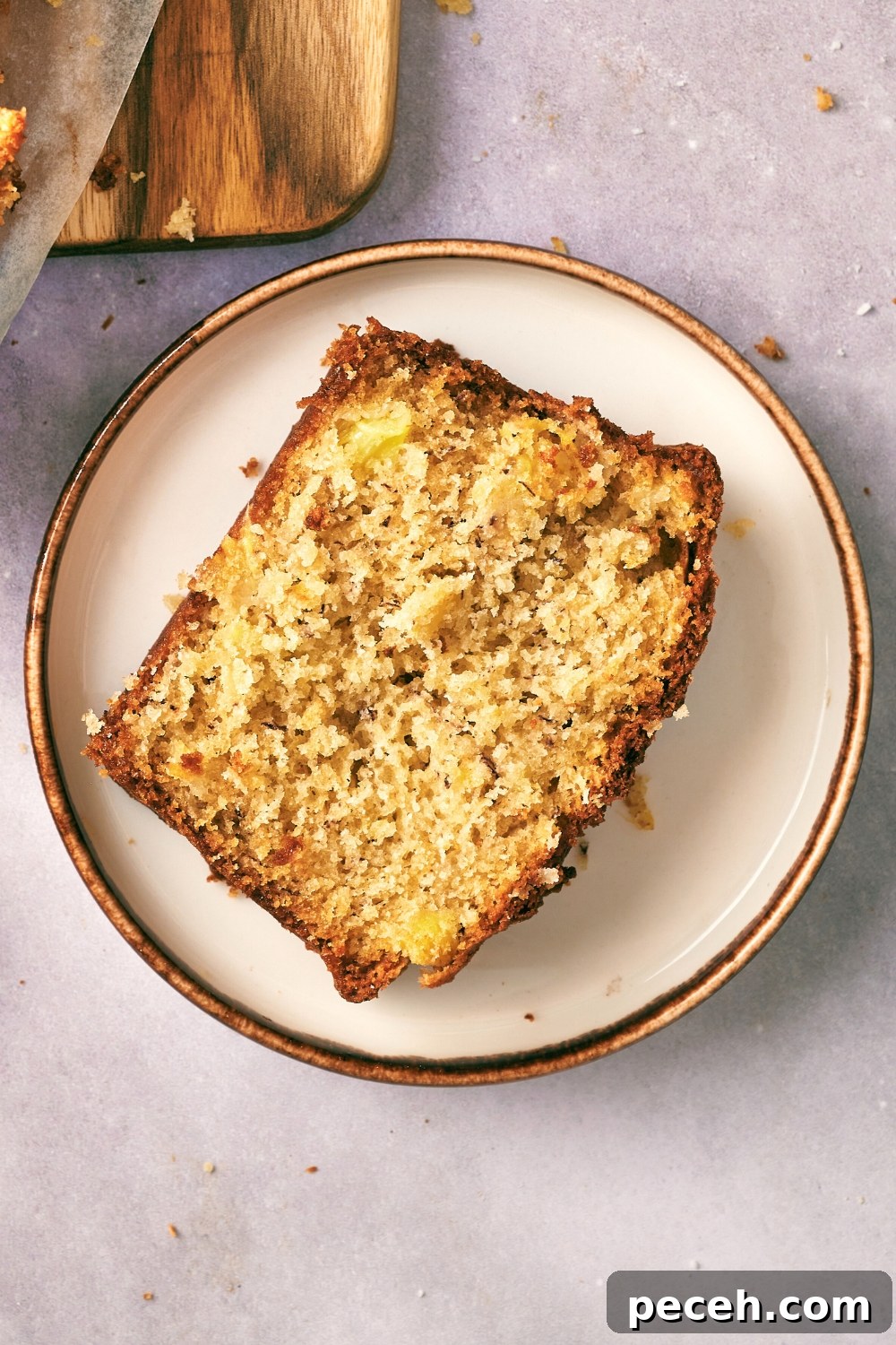 Tropical Hawaiian Banana Bread with Coconut and Macadamia Nuts 3 A slice of Hawaiian banana bread on top of a white plate on a grey counter.