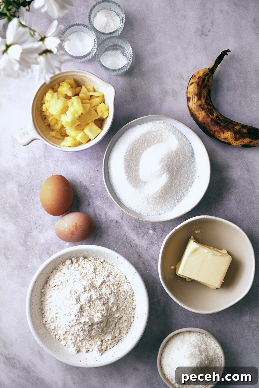 Tropical Hawaiian Banana Bread with Coconut and Macadamia Nuts 5 A countertop with a banana, pineapples, eggs, butter, flour, sugar, baking soda, baking powder, and salt all in separate bowls.