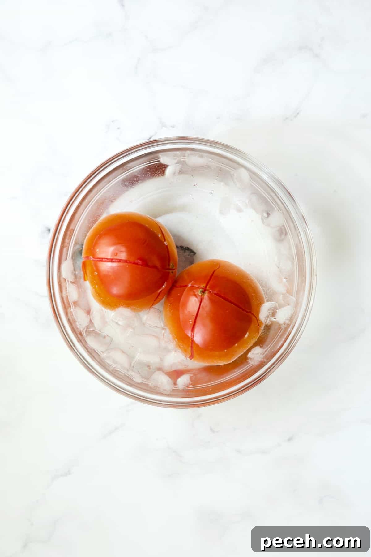 Two tomatoes in ice bath in glass bowl.