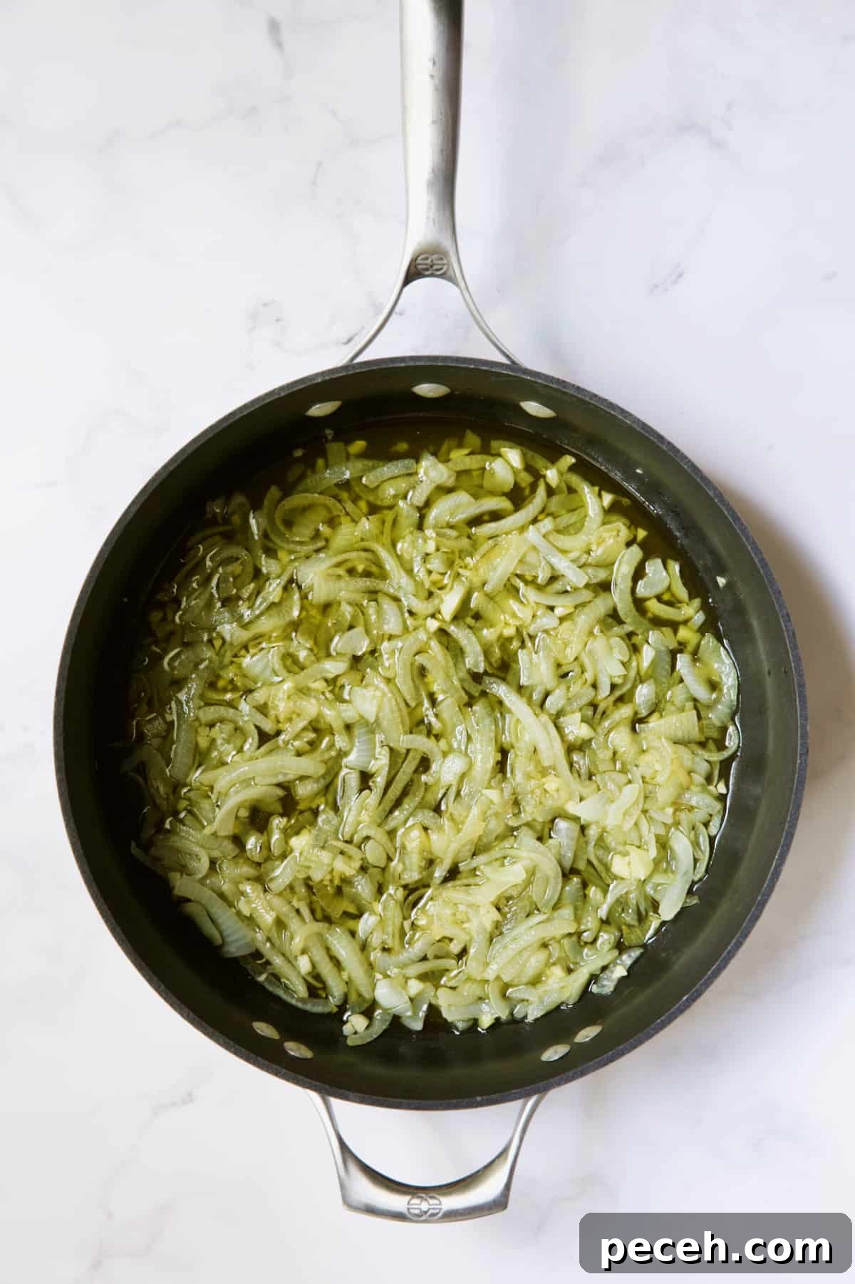 Onions being cooked in olive oil in skillet.