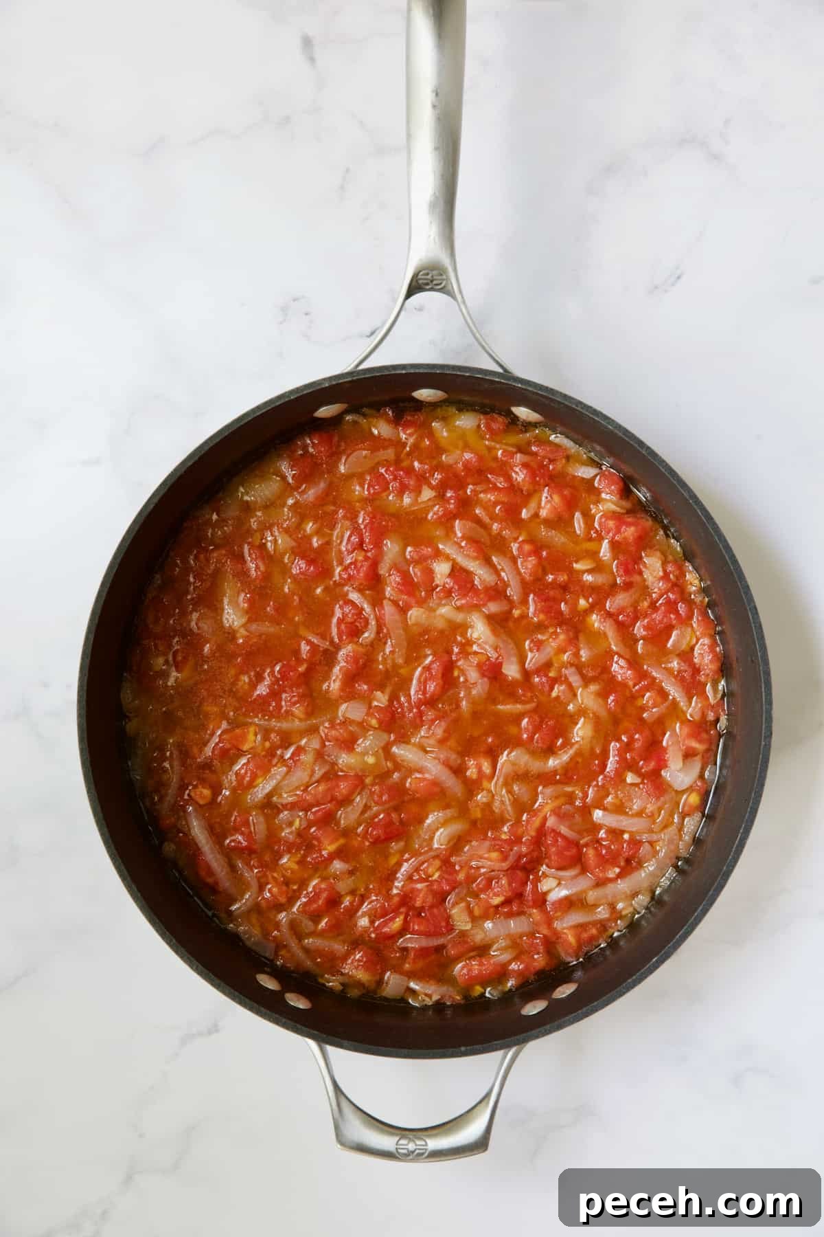 Tomatoes and onions being cooked in skillet.