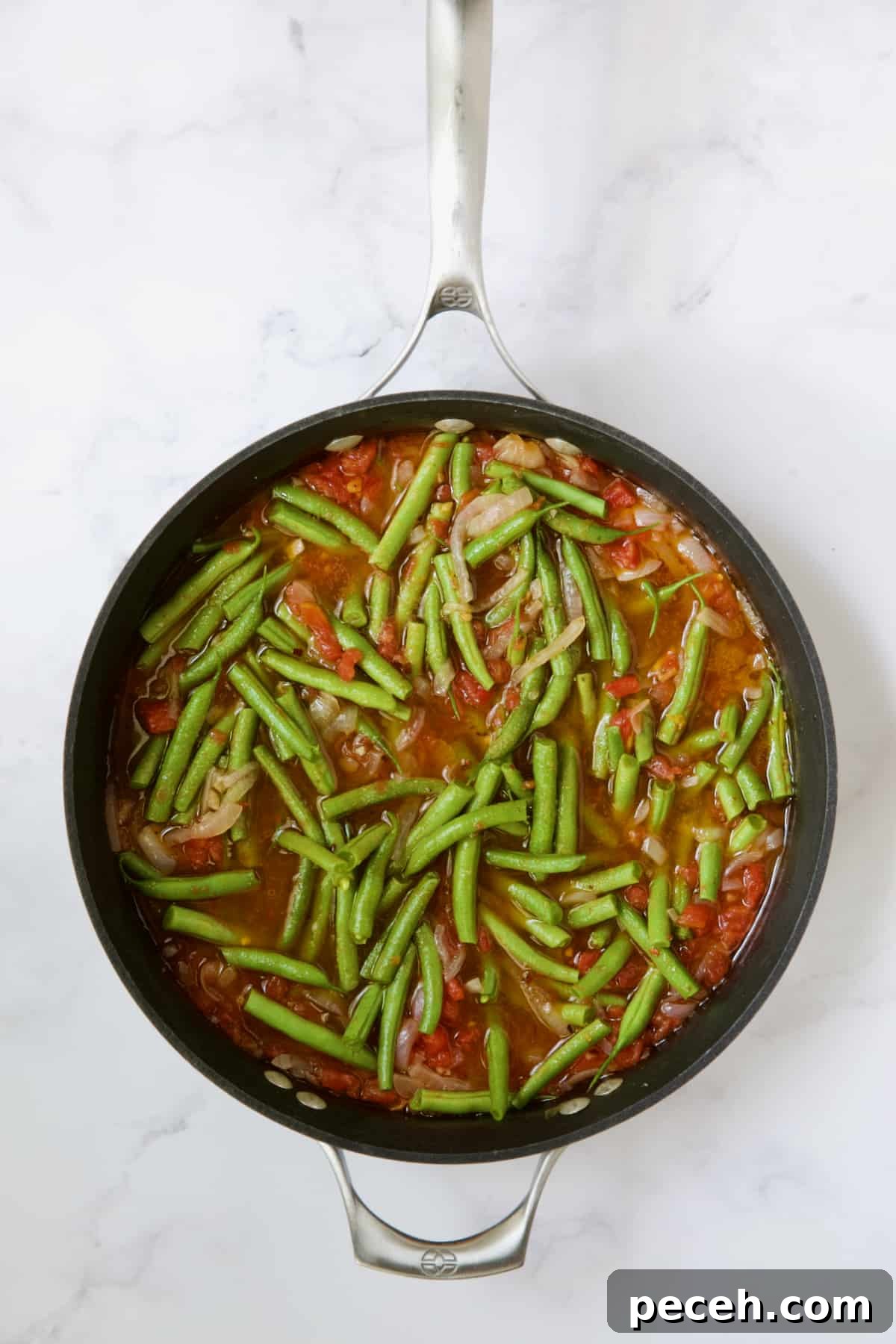 Green beans and tomatoes cooking in skillet right after fresh green beans are added.