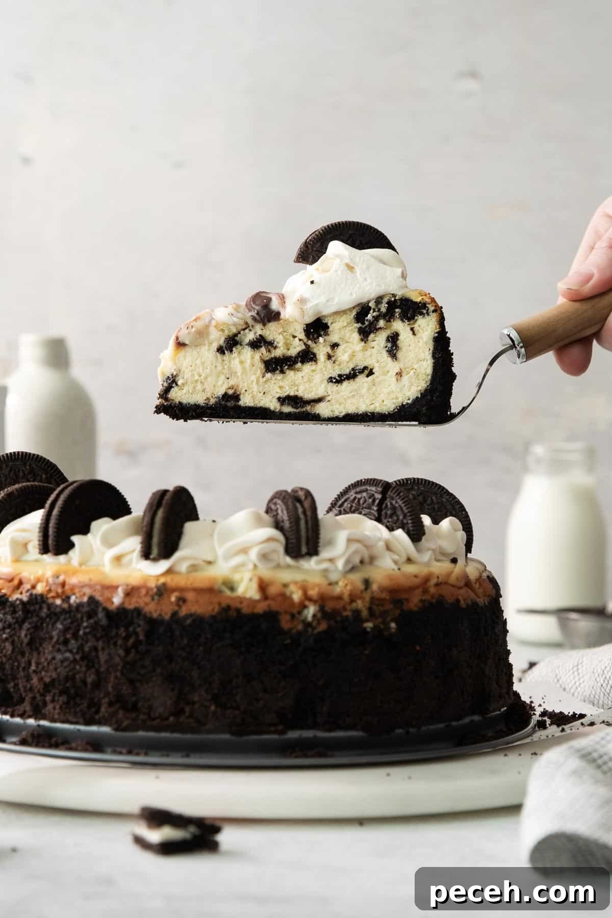 A hand lifting a slice of gluten-free Oreo cheesecake off of a platter
