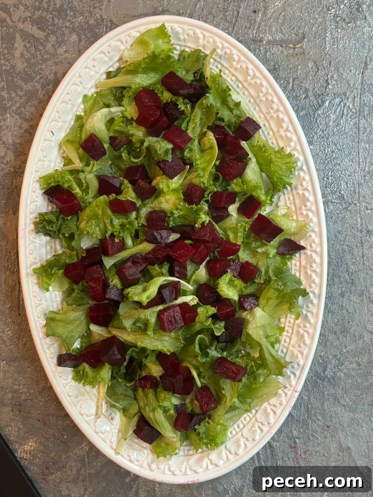 Roasted Beet Salad with Goat Cheese, Arugula and Walnuts 5 overhead image of a white oval platter topped with salad greens and diced cooked red beets