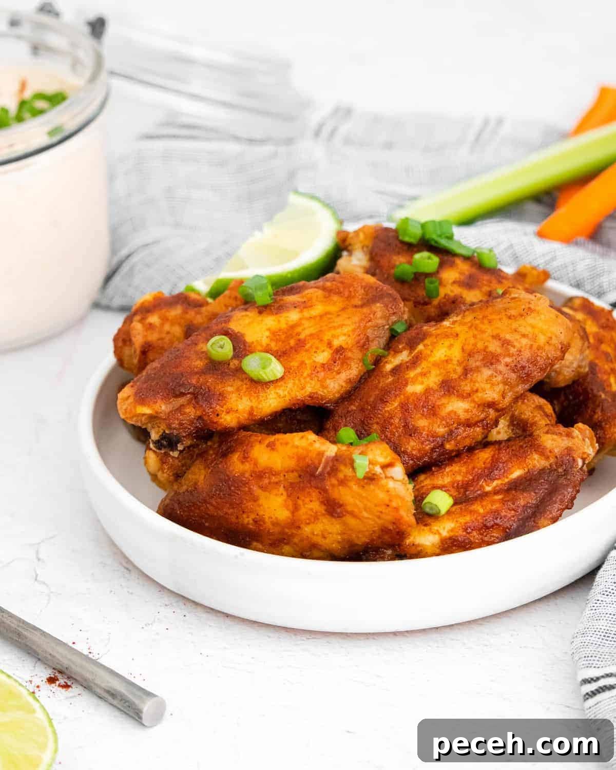 Chili Lime Chicken Wings with Tangy Dipping Sauce 2 Wings on a white plate, garnished with green onions and lime wedges.