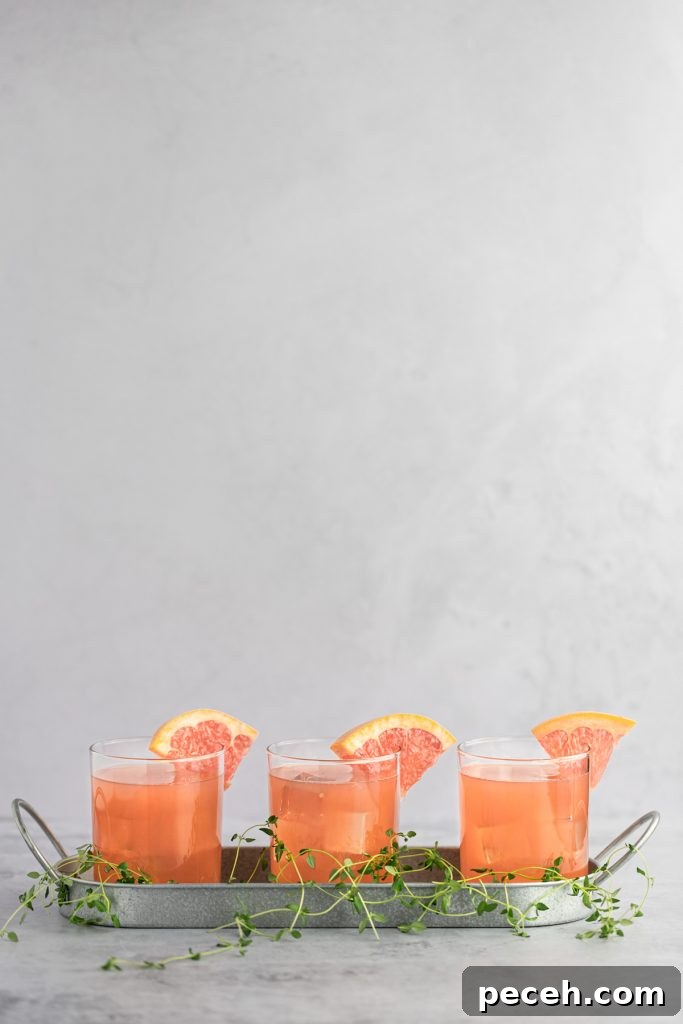 Sparkling Grapefruit Crush: Refreshing Citrus Cocktail Recipe 4 Three grapefruit cocktails beside each other in a metal tray, with fresh thyme scattered at the bottom.