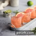 Three grapefruit crush cocktails on a metal serving tray, garnished with grapefruit, limes in the background.