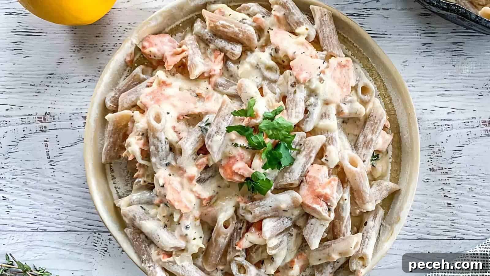 A plate of creamy pasta with salmon and a garnish of parsley on top, set on a white surface.