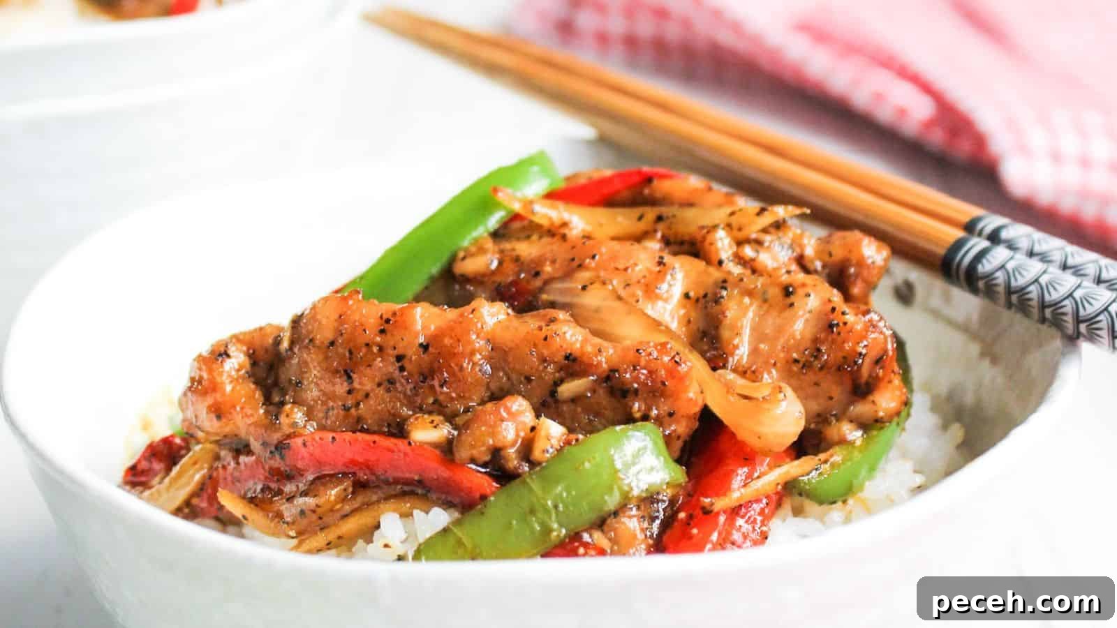 A bowl of chicken stir-fry with vegetables served over rice, accompanied by chopsticks.