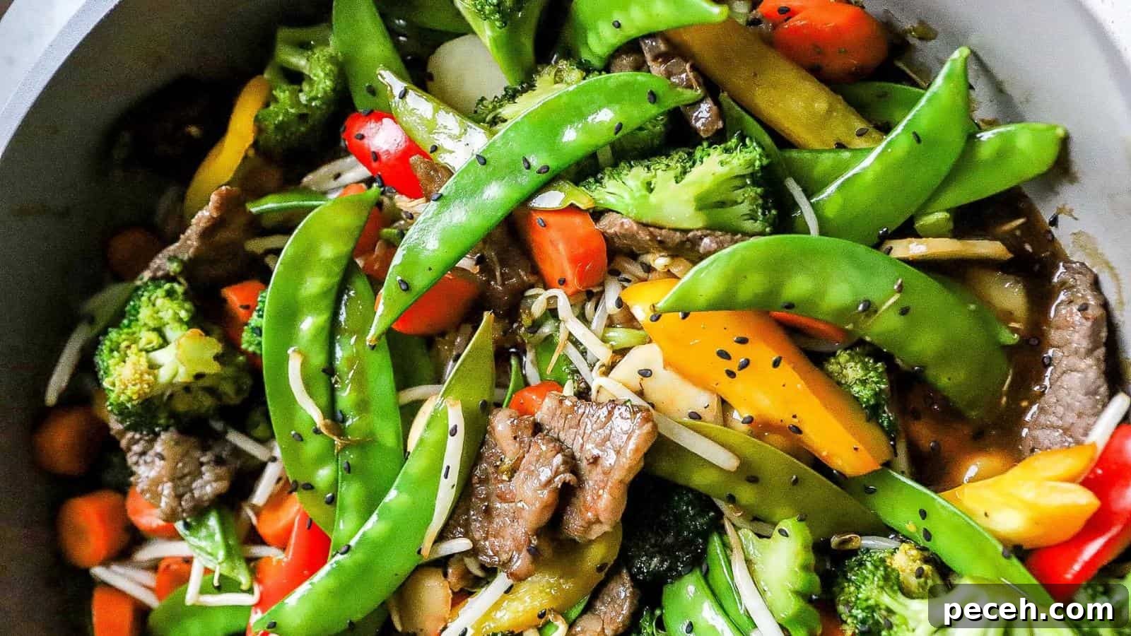Stir-fry dish with snap peas, broccoli, bell peppers, carrots, beef slices, and bean sprouts, topped with black sesame seeds.