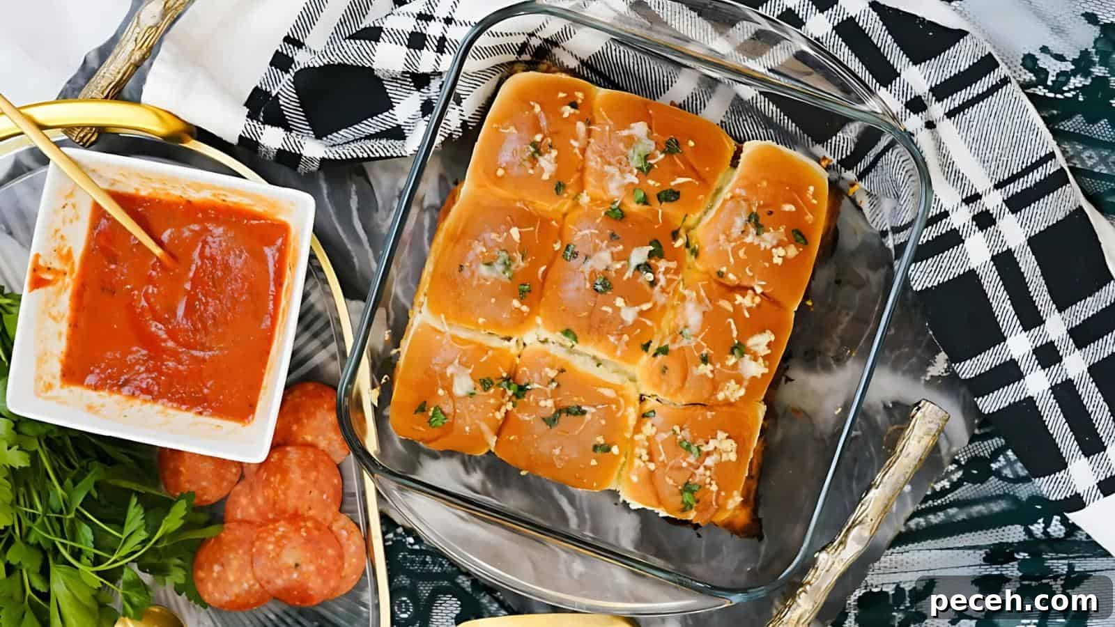 Glass dish with baked garlic bread rolls, garnished with herbs. Nearby, a bowl of tomato sauce, pepperoni slices, and parsley on a plaid cloth.