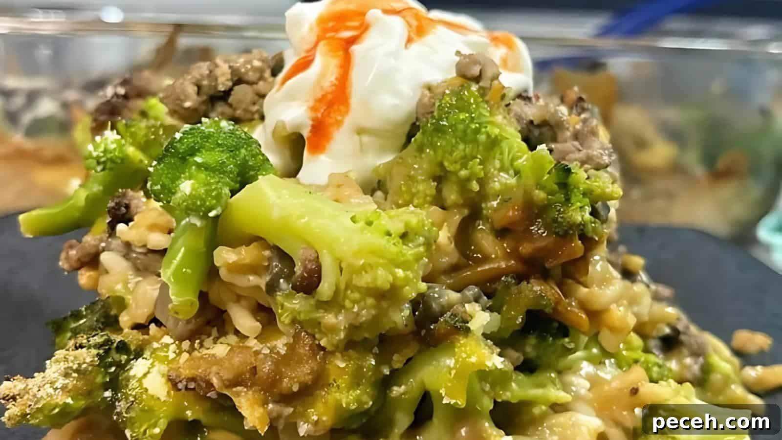 Close-up of a broccoli and ground meat casserole topped with a dollop of sour cream and a drizzle of hot sauce.